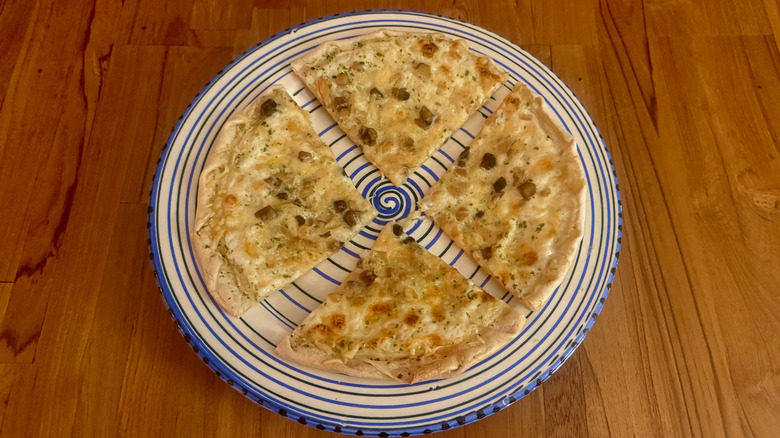 A small pizza with a thin crispy crust on a blue and white circular serving platter on a wooden table.