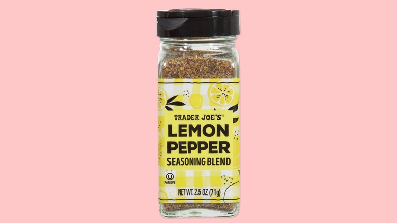A bottle of the new Trader Joe's Lemon Pepper Seasoning Blend on a salmon pink background.