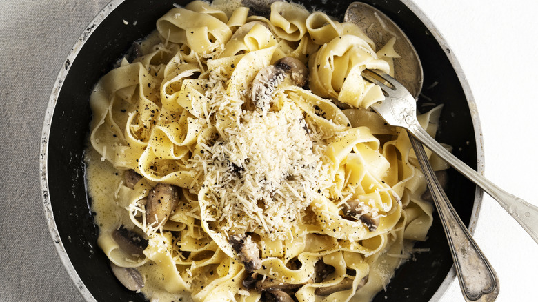 Pasta in a bowl tossed with parmesan with a fork and spoon.