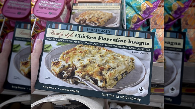 Hand holding box of Family Style Chicken Florentine lasagna over stocked TJ's freezer