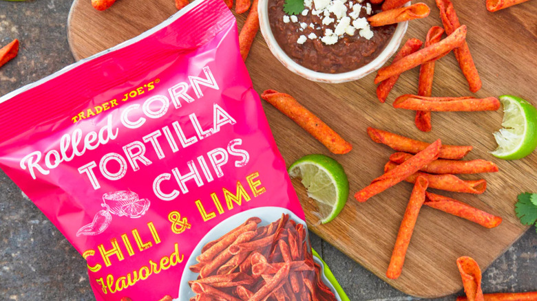 A bag of Trader Joe's Rolled Corn Tortilla Chips against a marbled surface near a cutting board with cut limes