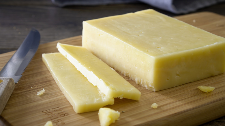 Sliced white cheddar cheese on cutting board with knife.