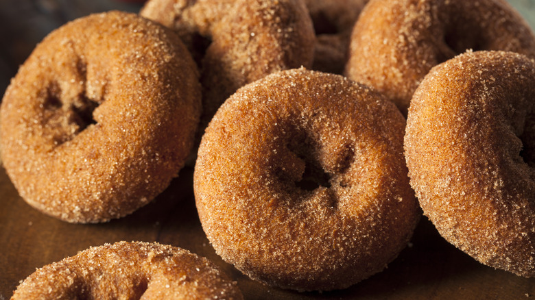 A pile of apple cider donuts on wooden surface.