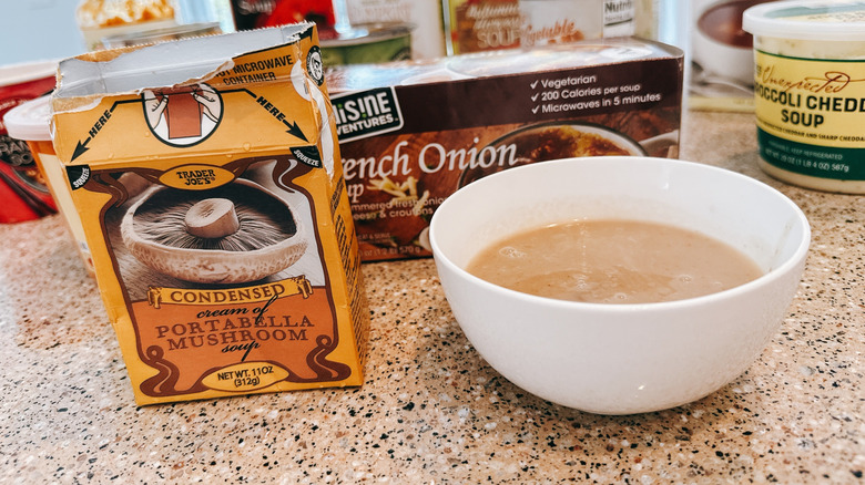 Box of Trader Joe's Condensed Portobello Mushroom soup next to some in a white bowl with other TJ's soups in background