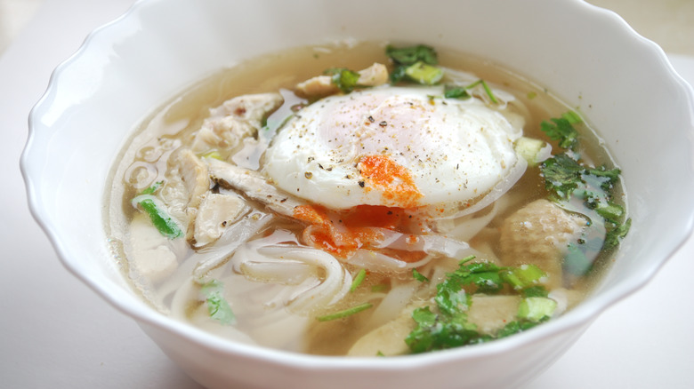 A bowl of Asian chicken and noodle soup topped with a soft-boiled egg in a white bowl