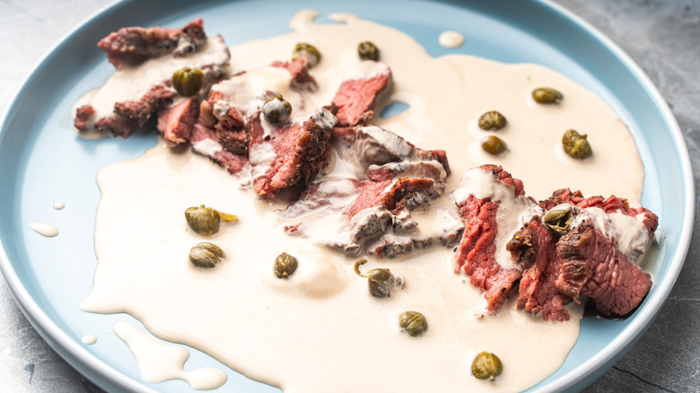 Pieces of beef smothered in a thin tonnato sauce on a blue plate
