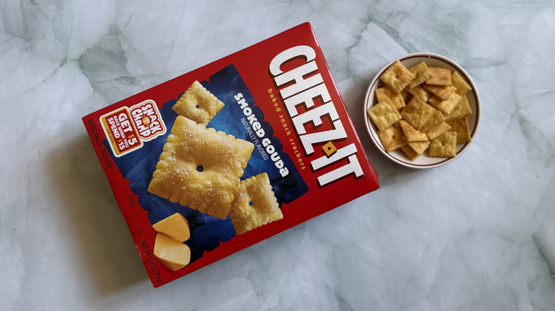 Cheez-It Smoked Gouda Snack Crackers laid on surface next to bowl of the Cheez-Its