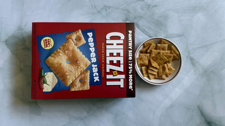 Box of Cheez-It Pepper Jack Snack Crackers laid horizontally next to bowl of the Cheez-Its