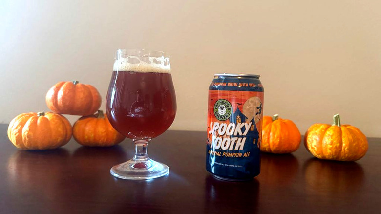 A full glass of beer next to a can of Spooky tooth pumpkin ale and five small pumpkins.
