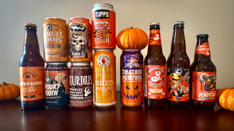 11 bottles and cans of pumpkin beer lined up on a wooden table with small pumpkins, including brands like Samuel Adams, Shipyard, and Tupps