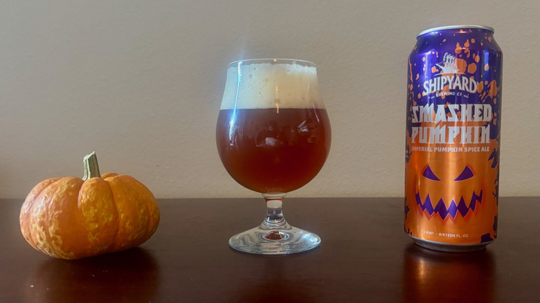 Shipyard Smashed Pumpkin tall beer can with a smiling jack-o-lantern next to a full beer glass and a small pumpkin.