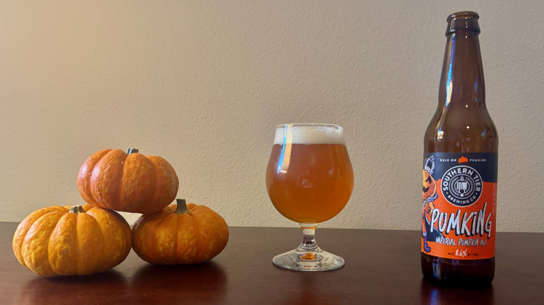 A goblet of orange-hued beer next to three small stacked pumpkins and a bottle of Southern Tier Pumking.