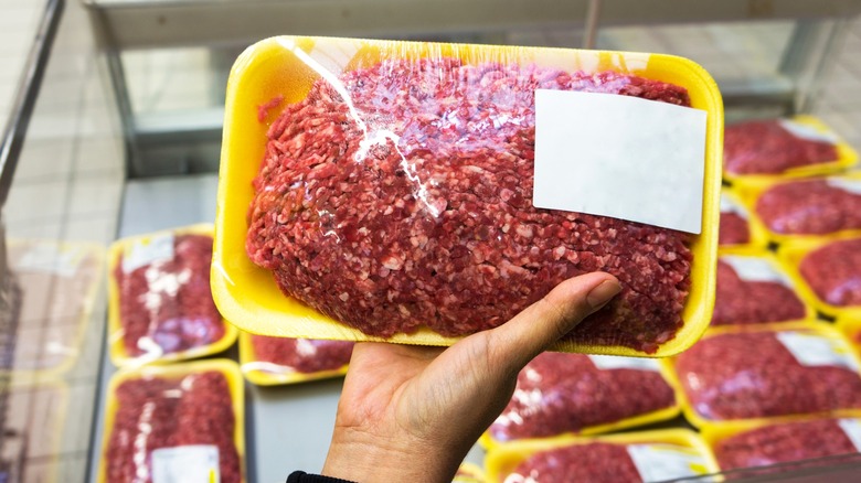 A person holds a package of ground beef in a grocery store