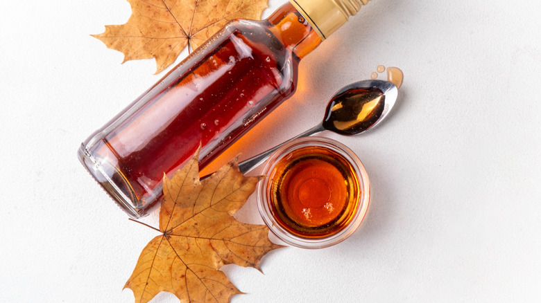 a bottle of fresh maple syrup with some maple leaves and a bowl of syrup