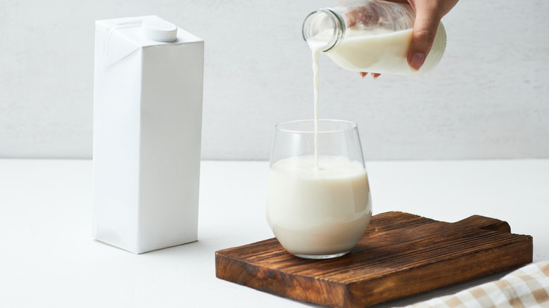 Pouring milk from a glass bottle into a glass on a wooden board