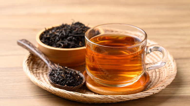 black tea in a glass mug with a bowl of tea leaves beside it