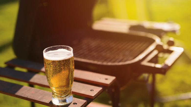 Glass of beer sitting on a side stand of a barbecue grill