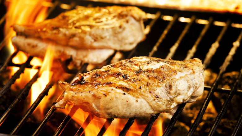 Chicken on barbecue grill with open flame.