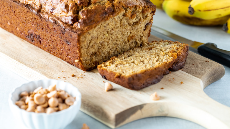 Banana bread loaf on board next to dish of brown baking chips