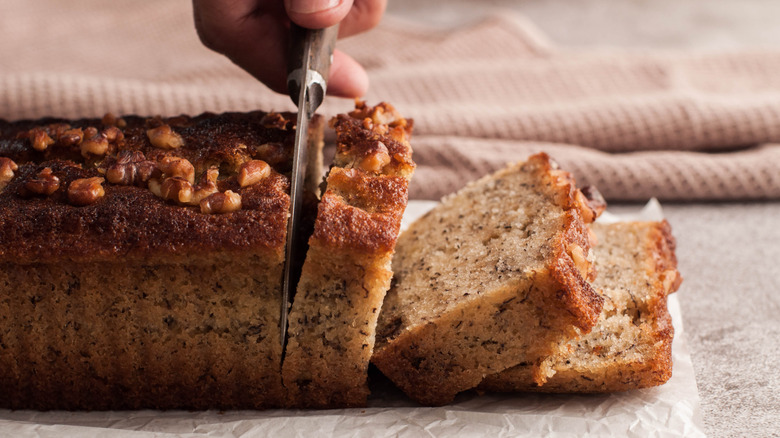 Hand slicing a loaf of banana nut bread on parchment