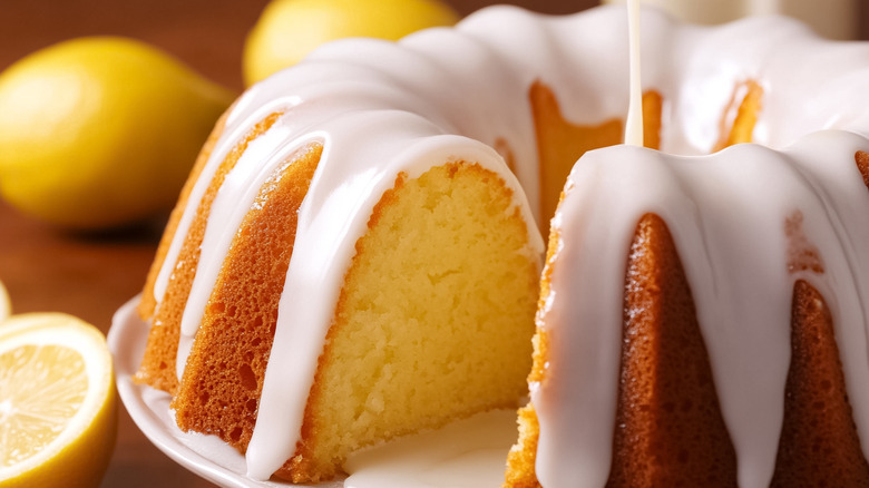 Lemon Bundt cake on a platter with lemons nearby and icing on top.