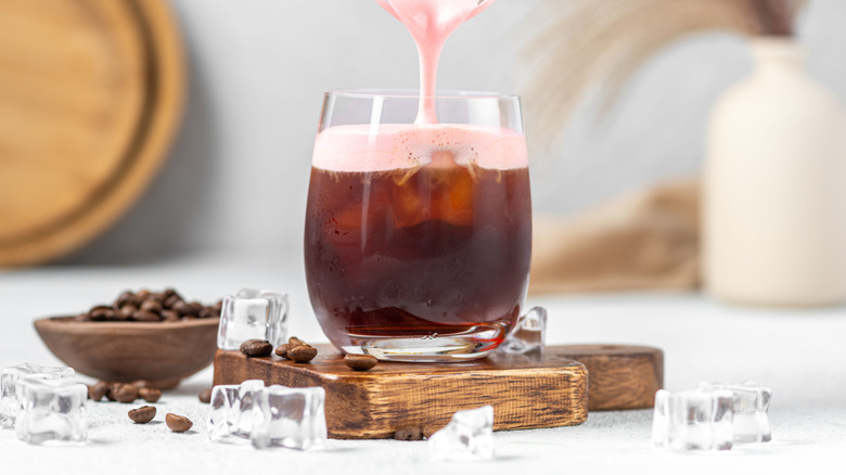 Pouring pink cold foam onto an iced coffee