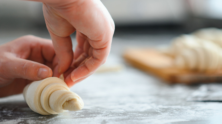 Hands rolling up crescent rolls on a floured surface