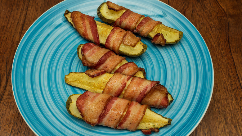 Pickle spears wrapped in bacon on a blue plate and wooden table.