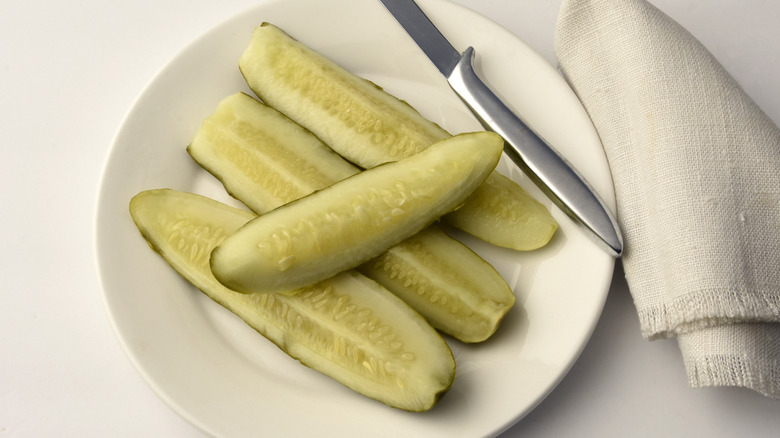 Pickle spears on a white plate with a knife and napkin to the side.