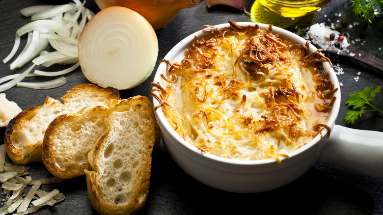 Toasted bread and sliced onion rests besides a crock of cheesy French onion cabbage soup