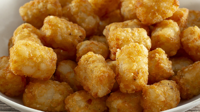 A white bowl filled with golden, crispy tater tots