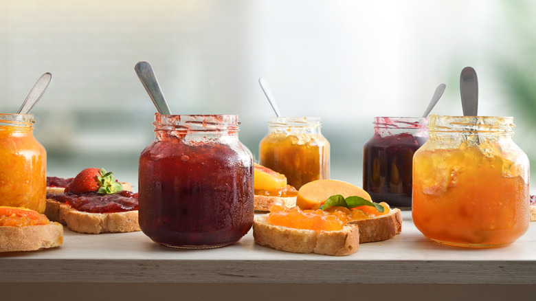 Glass jars of different flavors of jam including strawberry and peach with spoons