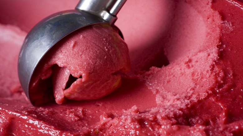 An ice cream scoop scooping some raspberry sorbet