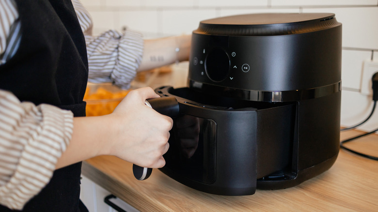 A person pulling out the tray of an air fryer