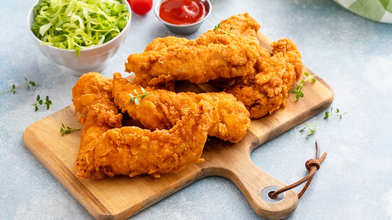 Fried chicken on a serving board next to lettuce and ketchup