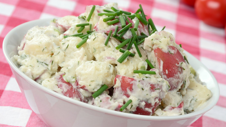 A freshly prepared potato salad made with red potatoes, mayonnaise, and fresh herbs on a red and white checkered tablecloth