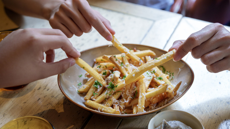 Friends sharing and enjoying fries topped with Parmesan cheese and truffled mayonnaise sauce.