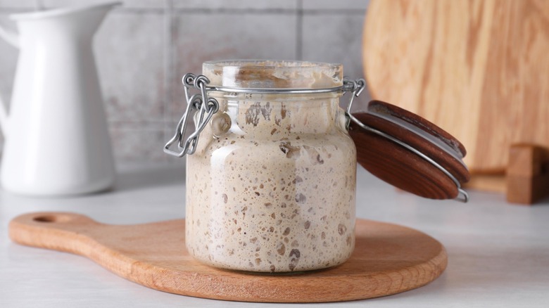 Sourdough starter in glass jar on a wood board on a kitchen counter.