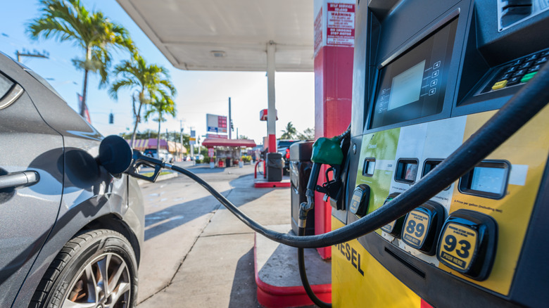 A gas station pump fueling a car on a sunny day with palm trees.