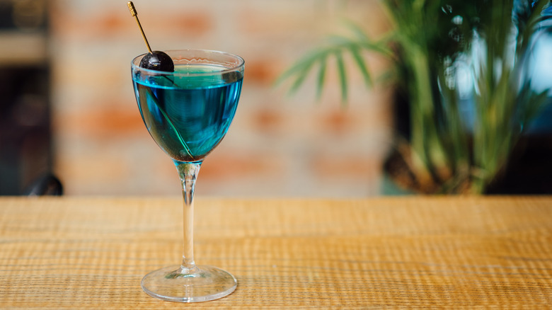 Aviation cocktail in a martini glass, garnished with a black cherry, captured in close-up.