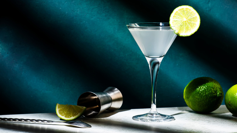 Vodka gimlet alcoholic cocktail with vodka, sugar syrup, lime juice and ice in martini glass, dark green background