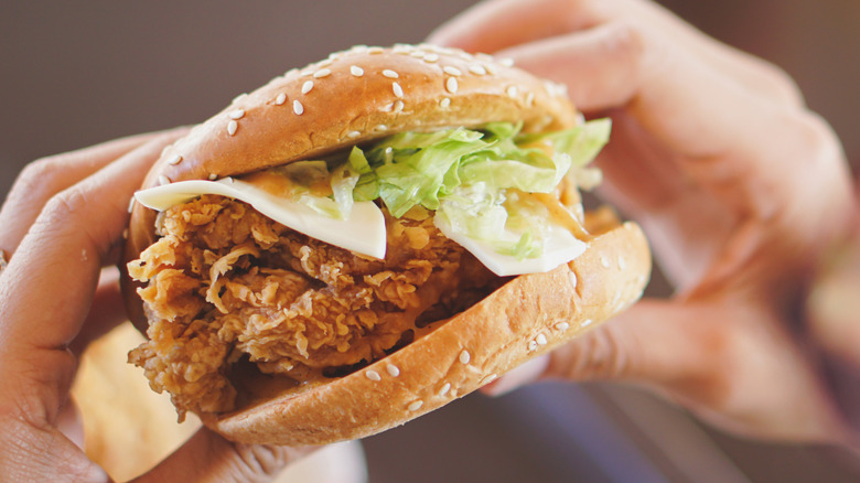 Holding a fried chicken sandwich with lettuce and cheese