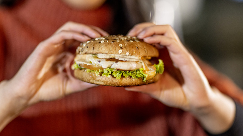 Woman in red sweater holds a fast food grilled chicken sandwich