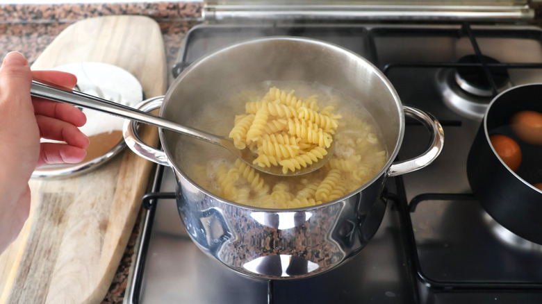 Scooping fusilli pasta from boiling pot of water