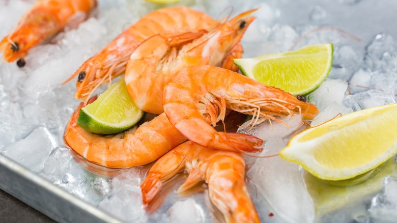 Several unpeeled shrimp laying in ice near wedges of lemon