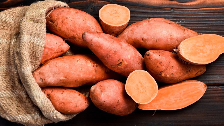 Burlap sack of raw sweet potatoes on wooden background