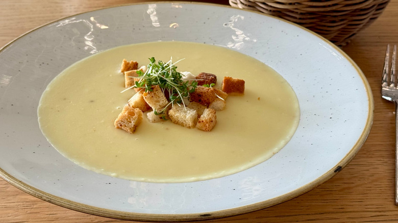 A speckled bowl of potato soup topped with croutons and sprouts