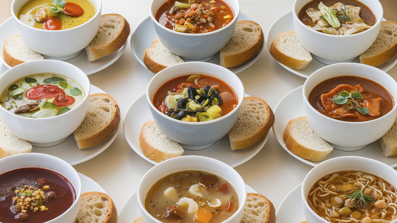Nine soup bowls filled with a variety of soups.