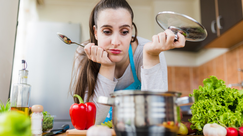Girl holding lid of pot looking down into pot with disappointed face