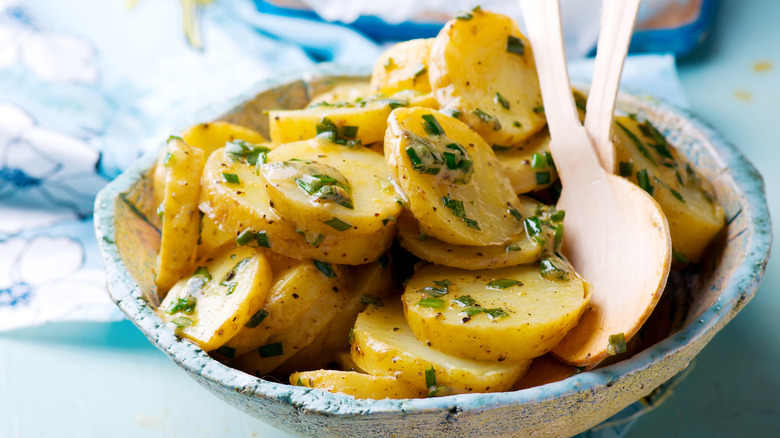 A bowl of potato salad with wooden utensils